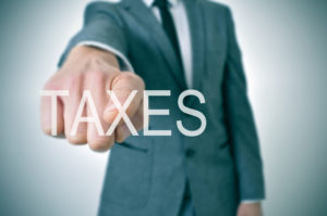 man wearing a suit pointing the finger to the word taxes written in the foreground